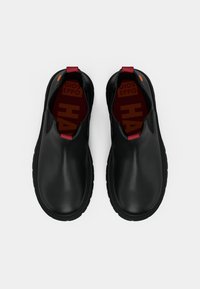Zapatos negros tipo slip-on con un acabado de cuero suave, que cuentan con una suela de goma, una pestaña roja y un acento naranja en contraste.