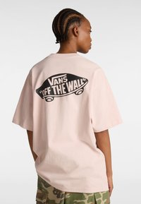 Rosa oversize t-shirt i bomull, med en svart "Vans Off The Wall" grafik på ryggen. Korta ärmar och avslappnad passform.