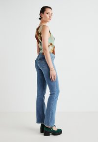 Večbarvna majica s tankimi naramnicami in tie-dye vzorcem, modri jeseni razširjeni jeans in zeleni platform čevlji iz semiša s podrobnostmi na sponki.