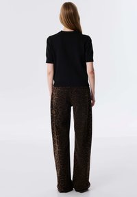Top nero a maniche corte abbinato a pantaloni larghi con stampa leopardata in tonalità marroni; presenta un orlo a costine e dettagli con tasche posteriori.