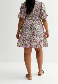 Blumenmuster-Hauskleid mit Rüschensaum. Verfügt über rosa und grüne Blumen auf schwarzem Hintergrund. Hergestellt aus leichtem Stoff mit kurzen Ärmeln.