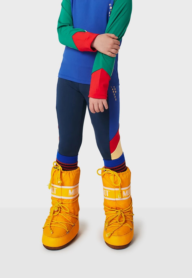Klart gula isolerade stövlar med vit branding, i kombination med en färgglad långärmad topp med blå, grön och röd ärm, samt marinblå leggings.