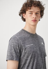 Grå kortermet trenings-T-skjorte laget av lett materiale, med en subtil tekstur og trykt "ADIDAS RUNNING"-logo på forsiden.