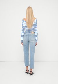 Ανοιχτό μπλε τζιν ψηλόμεσο με ευθεία γραμμή. Μία καφέ δερμάτινη ετικέτα είναι ραμμένη στη ζώνη πίσω. Μακρυμάνικη μπλούζα με ρίγες.