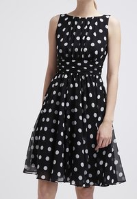 Robe noire sans manches avec des pois blancs, dotée d'un corsage ajusté et d'une jupe évasée, fabriquée en tissu léger avec une taille froncée.