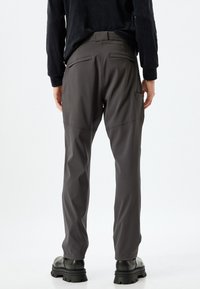 Pantalones de ejercicio gris claros, ligeros y elásticos con una textura suave, que cuentan con dos bolsillos traseros y un diseño ajustado. Llevados con botas negras de suela gruesa.