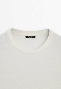Maglione bianco a collo rotondo realizzato in un tessuto morbido. Presenta un colletto e un orlo a costine. L'etichetta reca la scritta "Massimo Dutti", indicando l'origine del marchio.