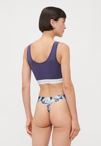 Lilla sømløs bralette med bred hvit elastisk band, sammen med blå og kremfarget blomstermønstrede stringtruser. Materialet ser mykt og elastisk ut.