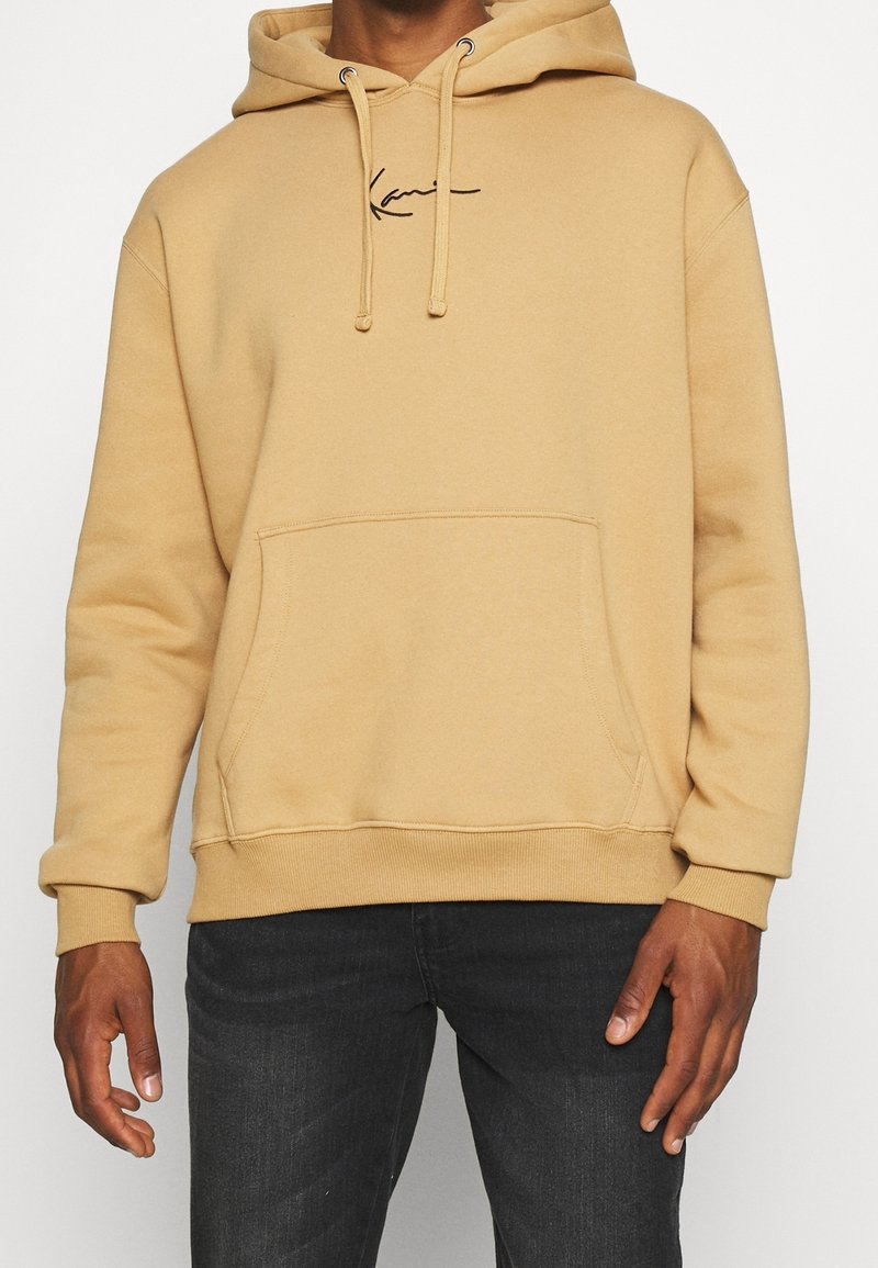 Felpa con cappuccio beige in cotone con tasca a marsupio frontale e coulisse. Presenta un logo nero ricamato sul petto e polsini a costine.