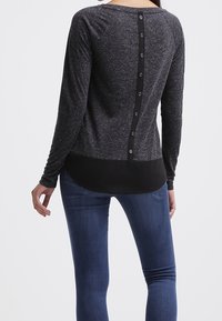 Langarmshirt aus dunkelgrauem strukturiertem Stoff, mit schwarzem Einsatzsaum und einem Knopfdetail entlang der Mitte des Rückens.