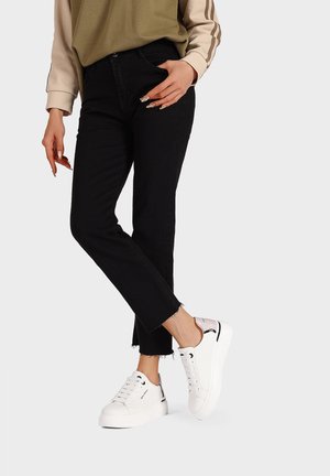 Jeans neri a vita alta con orli sfilacciati abbinati a sneaker bianche con un design testurizzato e accenti a contrasto.