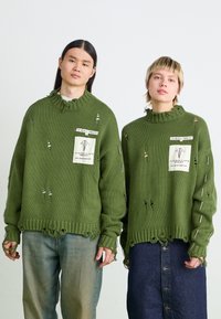 Pulls en maille surdimensionnés couleur vert olive avec un ourlet effiloché, ornés de déchirures et d'accents de pince de sûreté, présentant une étiquette en patch à l'avant.