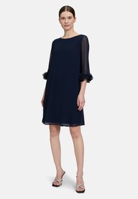 Robe bleu marine à coupe ample, manches transparentes et accents froncés aux poignets. Fabriquée en tissu léger avec un col rond.