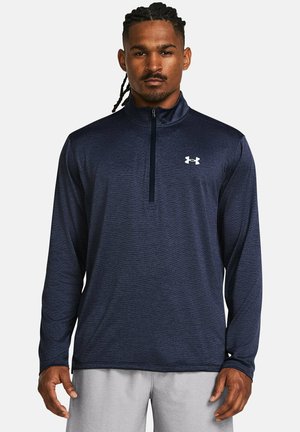 Camisa atlética de manga larga en color navy, hecha de tela texturizada, con cuello de media cremallera y un logo blanco en el pecho.