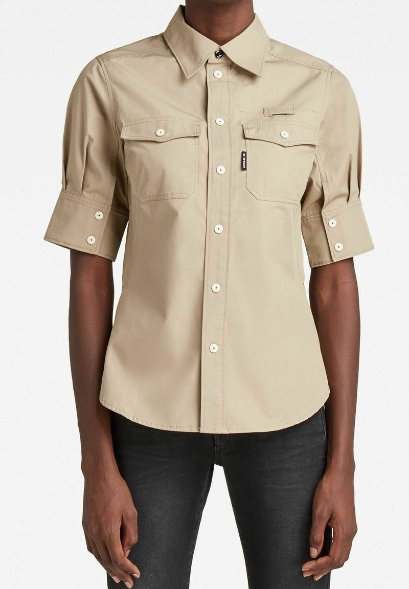 Ljusbeige kortärmad skjorta med krage, två bröstfickor, knapplist fram och uppvikta manschetter. Har en texturerad tyg och subtil sömnad.