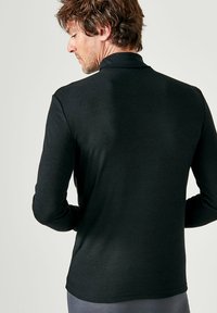 Zwarte longsleeve polo t-shirt gemaakt van zachte stof, met een gestructureerde kraag en een slim fit. Zichtbare stiksels op de mouwen en de zoom.