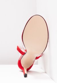 Sandale à talons hauts en suède rouge avec une bride transparente. Présente un bout pointu et une semelle lisse, montrant le côté intérieur et le talon.