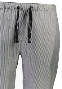 Close-up van grijs en witte gestreepte pantalon met een elastische tailleband en zwarte trekkoorden met witte en blauwe stiksel.