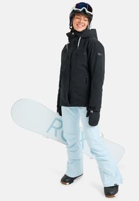 Black snow jacket with zip pockets, light blue snow pants, black gloves, and a white snowboard with blue lettering. Helmet with goggles.