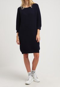Abito a maglia a coste blu navy con maniche a tre quarti e scollo rotondo, caratterizzato da una vestibilità ampia e spacchi laterali all'orlo.