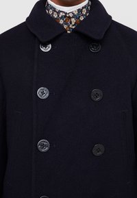 Cappotto peacoat in lana blu navy con design doppiopetto, grandi bottoni neri e colletto. Presenta cuciture sottili e tasche laterali.