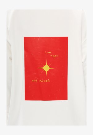 Żółta gwiazda wybuchu i ręcznie napisany tekst "Jestem magią i cudem" na czerwonym kwadracie umieszczonym na białym tle tkaniny.