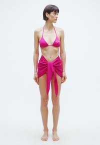 Rózsaszín bikini szett háromszög felsőrésszel és hozzáillő, derekán megkötött szoknyával. Az anyag simának és rugalmasnak tűnik, úszáshoz alkalmas.