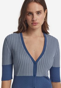 V-ringad kardiagan i ljusblå och mörkblå ribbad stickning. Korta ärmar, två knappar framtill, subtil textur och färgblockerat mönster.