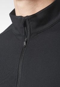 Acercamiento del cuello de una chaqueta negra con cremallera parcialmente cerrada, mostrando la textura de la tela y los detalles de la costura.