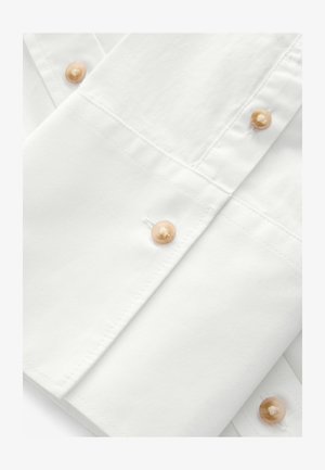 Biela košeľa s viditeľným šitím a krémovými gombíkmi. Hladký povrch, s klasickým golierom a légou. Minimalistický dizajn.