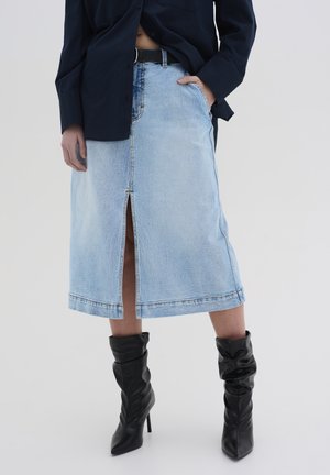 Gonna midi in denim blu chiaro con spacco frontale e cuciture a contrasto, abbinata a stivali neri al ginocchio, morbidi con tacco e una camicia scura.