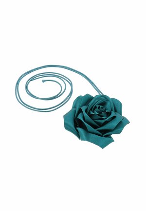 Rose en tissu bleu sarcelle attachée à un long cordon assorti de la même couleur, enroulé à côté de la fleur sur un fond blanc.
