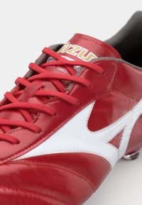 Clé de soccer rouge avec une finition en cuir brillant. Présente des accents blancs, des lacets texturés et un logo sur la languette. Conçue pour la performance.