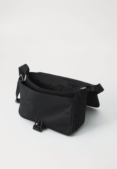 Black crossbody bag made of smooth, water-resistant fabric. Features a structured shape, adjustable strap, and a front pocket with a clip closure.