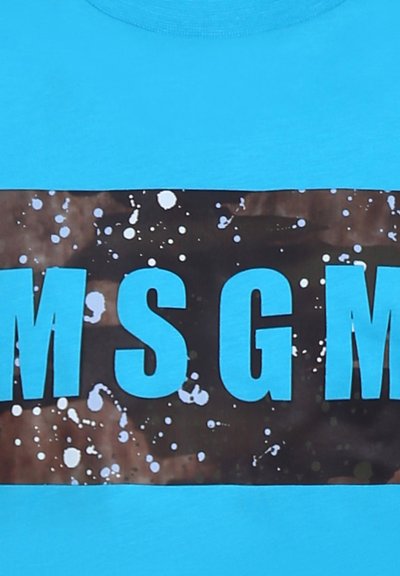 Maglietta di cotone turchese con una grande grafica nera con testo blu "MSG" e motivi di spruzzi bianchi nella zona centrale.