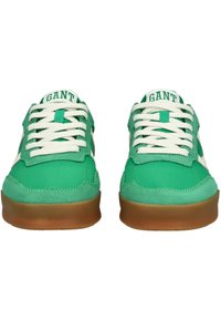 Sneakers in suede verde con lacci bianchi e suola in gomma marrone. Presentano una toppa con logo sulla linguetta e accenti bianchi a contrasto sui lati.