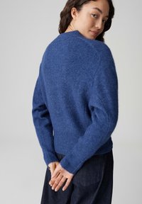 Maglione blu in lana con una texture morbida, orlo a coste e maniche ampie. Visualizzato dalla parte posteriore, presenta una vestibilità rilassata e una scollatura classica.