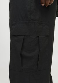 Pantalones cargo negros con un gran bolsillo lateral con pliegues, fabricados con una tela texturizada, diseño ajustado y un brillo sutil.
