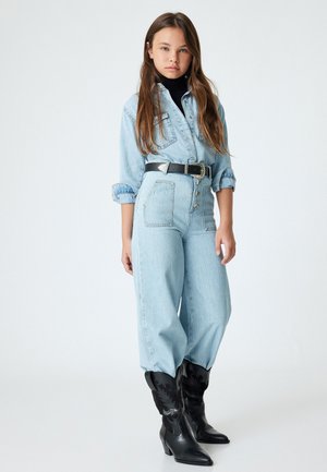 Chaqueta de mezclilla azul claro y jeans de cintura alta con cinturón negro; combinados con botas de vaquero negras con diseño texturizado y puntera puntiaguda.
