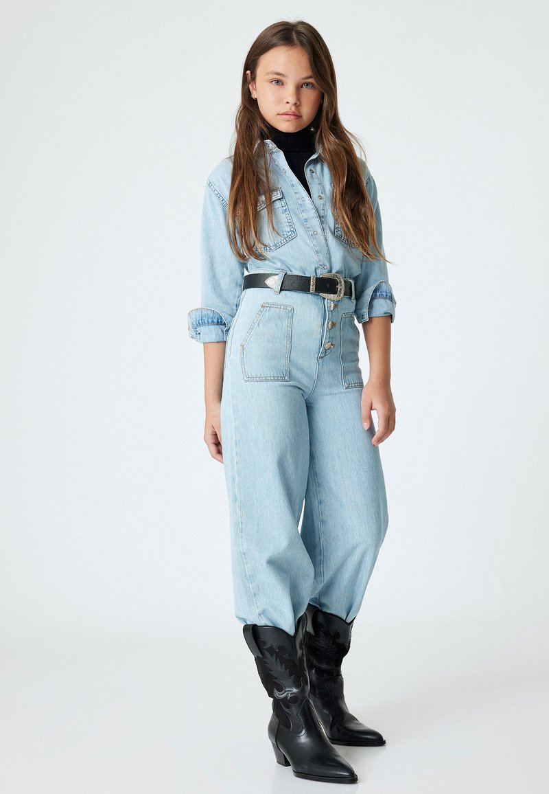 Chaqueta de mezclilla azul claro y jeans de cintura alta con cinturón negro; combinados con botas de vaquero negras con diseño texturizado y puntera puntiaguda.