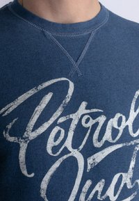 Sudadera de algodón azul con cuello redondo acanalado, que presenta un diseño gráfico de texto blanco desgastado. Detalles de costura visibles en el cuello.