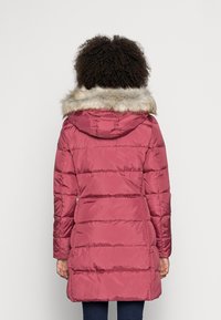 Abrigo acolchado en rosa oscuro con capucha de piel sintética. Presenta costuras horizontales y mangas largas, que llegan hasta la mitad del muslo.