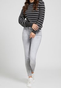 Maglione a righe grigie con polsini a coste, abbinato a jeans skinny grigio chiaro e scarpe da ginnastica bianche. Tessuto morbido, design aderente, stile casual.
