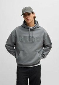 Grijze sweatshirt met een capuchon en groot "HUGO" logo op de voorkant. Heeft een kangoeroezak en geribbelde manchetten voor een relaxte pasvorm.