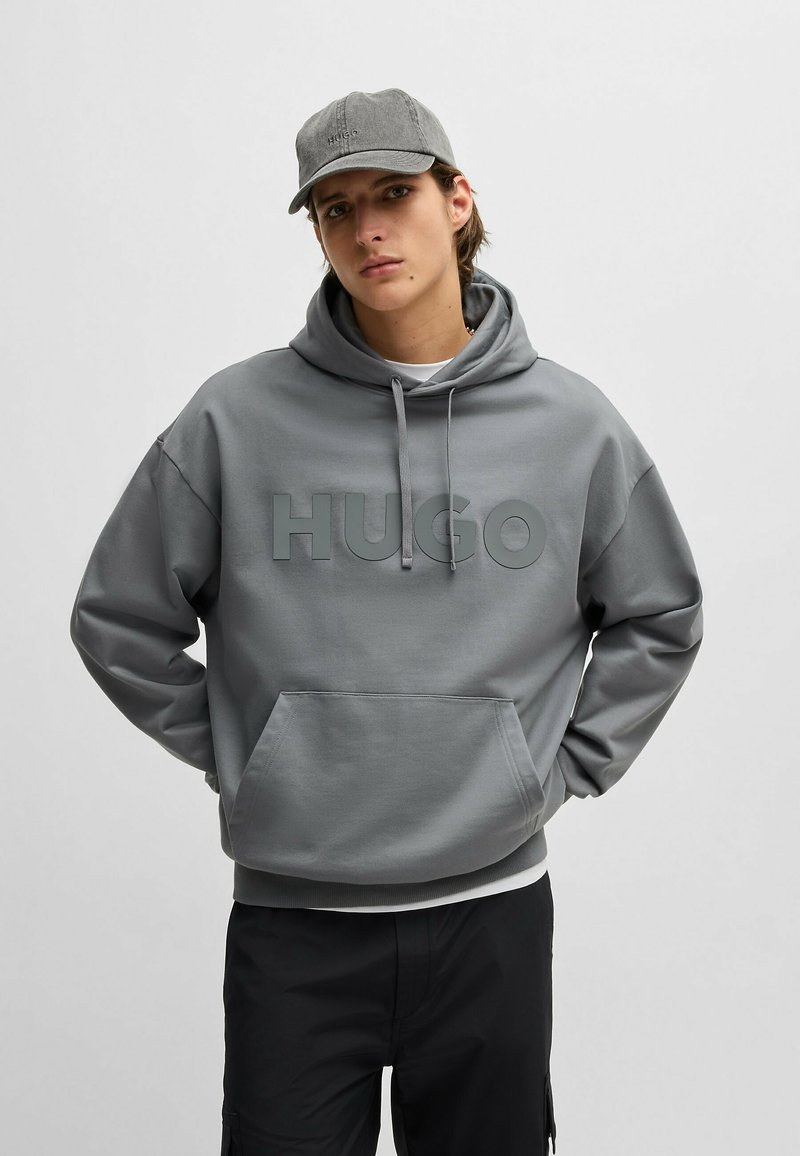 Grå sweatshirt med huva och stor "HUGO"-logotyp på framsidan. Har en känguruficka och ribbade ärmslut för en avslappnad passform.