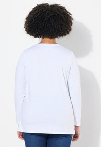 Langärmliges weißes T-Shirt aus Baumwolle; mit rundem Halsausschnitt und leicht lockerer Passform; glatte Textur ohne sichtbare Muster oder Akzente.