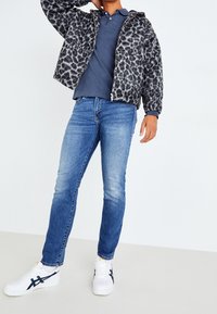 Chaqueta polar gris con estampado de leopardo, camisa polo azul marino, vaqueros azules y zapatillas blancas con detalles en azul marino. Diseño ajustado con material texturizado.