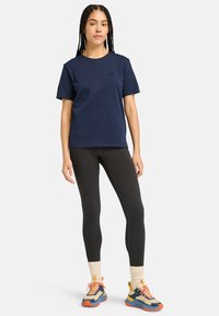 T-paita tummansinisestä puuvillasta, jossa on lyhyet hihat ja logo. Yhdistetty mustiin legginseihin ja monivärisillä yksityiskohdilla varustettuihin sneaker-kengiin, joissa on neulotut hihnat.