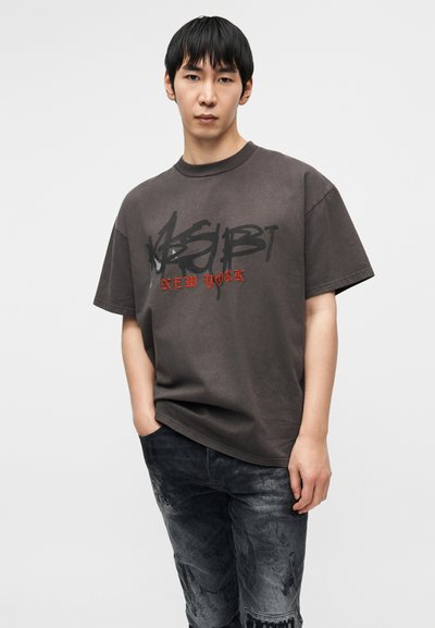 Παντελώς μεγάλο μπλουζάκι σκούρου γκρι με γραφικά μαύρα και κόκκινα γράμματα που γράφουν «NEW YORK», σε συνδυασμό με μαύρο distressed τζιν. Κοντά μανίκια, στρογγυλή λαιμόκοψη.