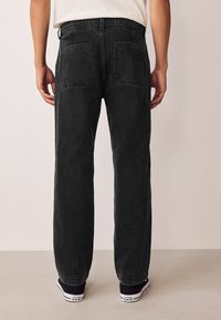 Schwarze Jeans aus Denim mit geradem Bein, ausgestattet mit doppelten Gesäßtaschen und einer dezenten Textur, kombiniert mit marineblauen Sneakers.